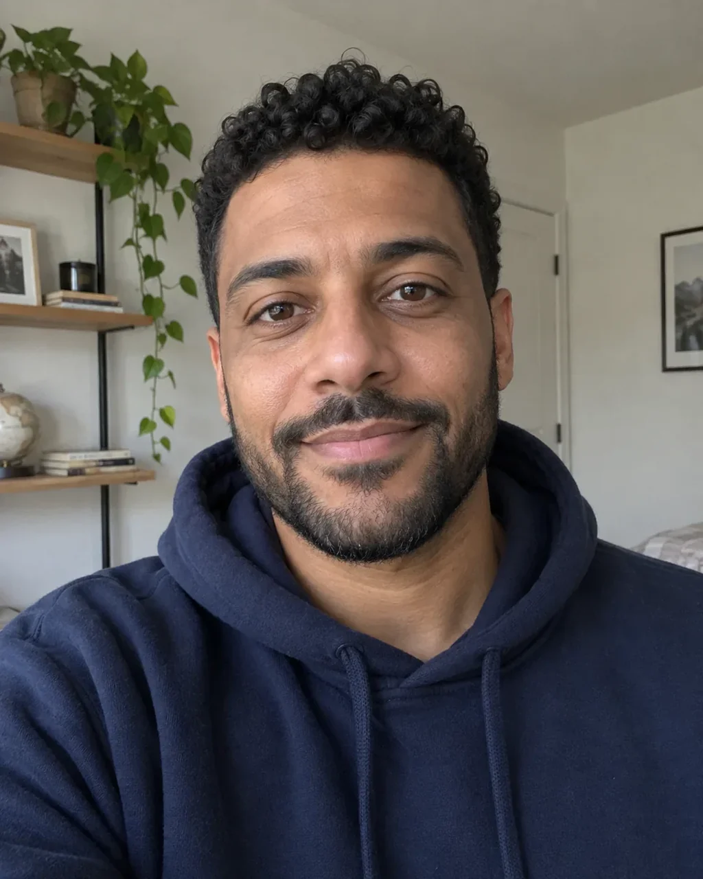 Man in a navy hoodie taking a selfie in front of shelves